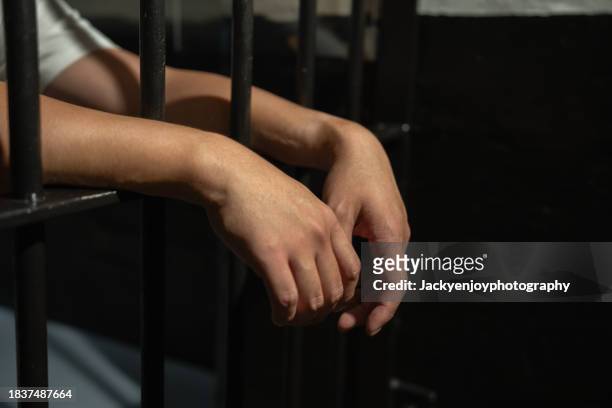 hands of a prisoner in a cell behind bars. - häftling stock-fotos und bilder