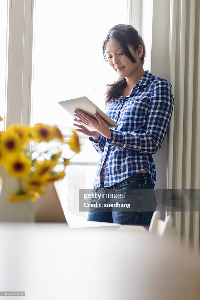 Woman using digital tablet beside window