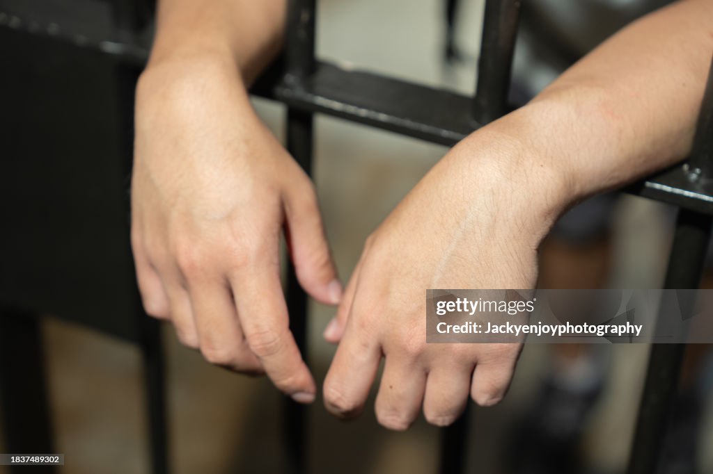 Hands of a prisoner in a cell behind bars.