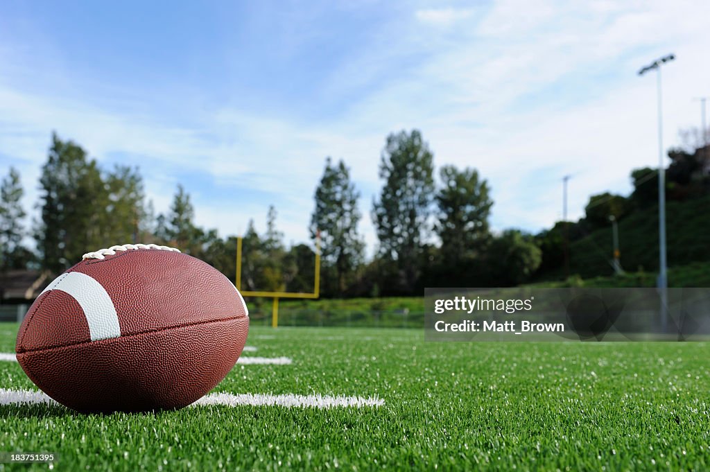 Close-up of a football on a field with view of the goalpost