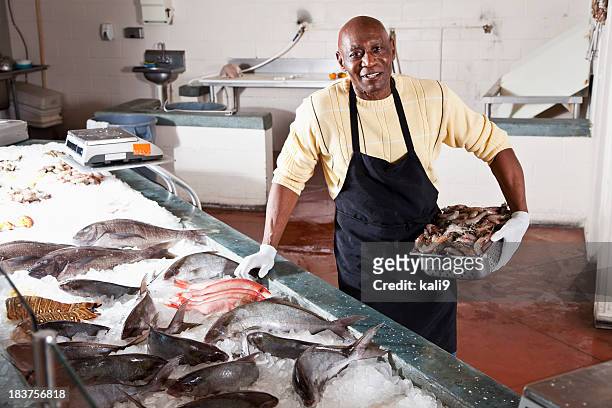worker in seafood market by fresh fish display - fishmonger stock pictures, royalty-free photos & images