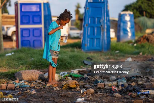 poverty , poor, black african child brushing her teeth next to portable toilets and stinking effluent water in an informal settlement - bidonville photos et images de collection