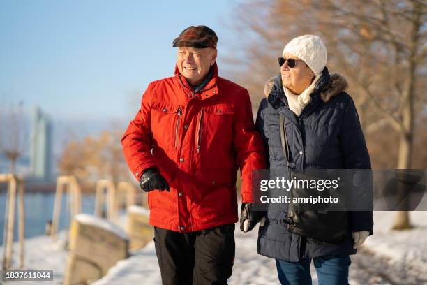 active senior couple on winter walk close to river on sunny day with snow - snow day stock pictures, royalty-free photos & images