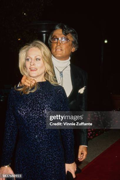 American actress Beverly D'Angelo, wearing a black-and-blue dress, and American film producer and actor Robert Evans, who wears a black jacket over a...