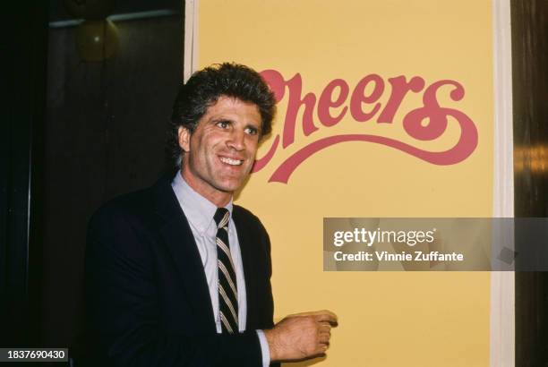 American actor Ted Danson wearing a dark blue blazer over a light blue shirt with a dark blue, white and red diagonally-striped tie, pointing to a...
