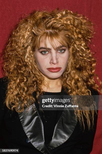 American singer and songwriter Taylor Dayne, wearing a black jacket with black silk lapels, poses against a red background, United States, circa 1990.