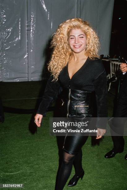 American singer and songwriter Taylor Dayne, wearing a black top with a high-waisted black leather skirt, walking before a backdrop which reads...