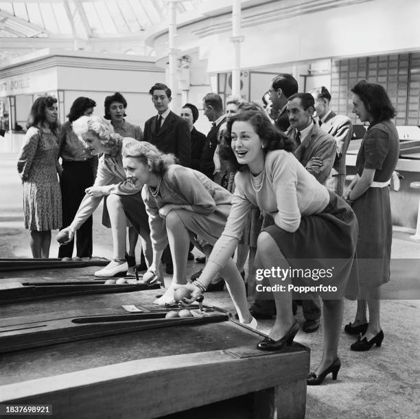 From left, Josephine Harris, Iris Kinipple and Joy Theelke play an arcade game on Palace Pier in the seaside town of Brighton in Sussex, England on...