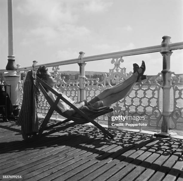 Woman sunbathes seated in a deckchair on Palace Pier in the seaside town of Brighton in Sussex, England on 2nd July 1946.