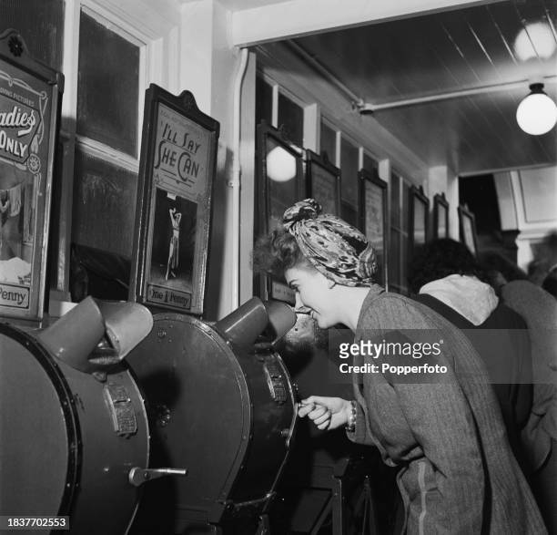 Woman pays a penny and winds a handle to watch a motion picture on a coin operated Mutoscope device in an amusement arcade on Palace Pier in the...