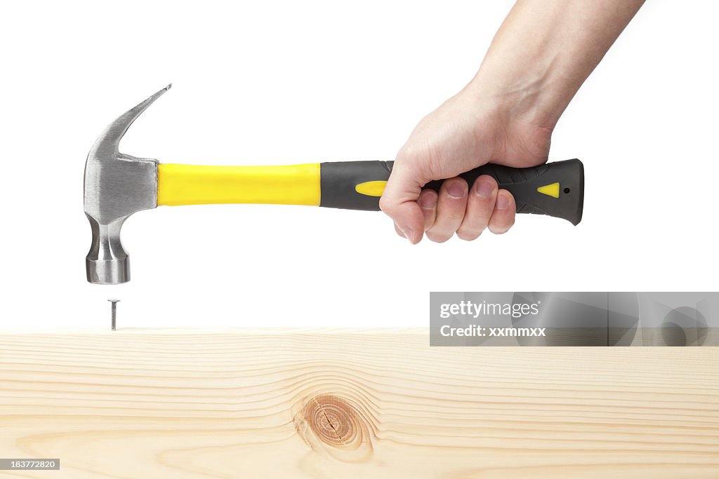 Hand holding hammer hitting a nail in wood