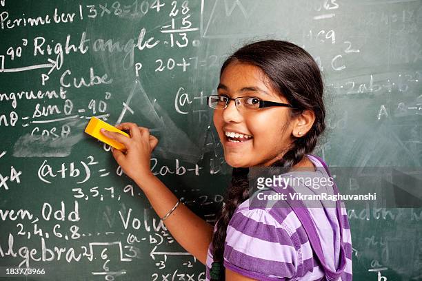 cheerful indian girl student erasing mathematics problems from greenboard blackboard - girls stock pictures, royalty-free photos & images