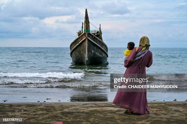 Woman with her child looks at a boat which carried Rohingya refugees to the Laweueng beach in Pidie district of Aceh province, on December 10, 2023....