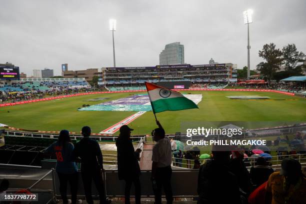 An India supporter waves a flag while covers are visible on the pitch as rain has delayed the start of play ahead of the first T20 cricket match...