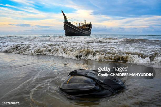 An abandoned bag lies on beach sand as waves lash a boat which carried Rohingya refugees to Laweueng beach in the Pidie district of Aceh province, on...