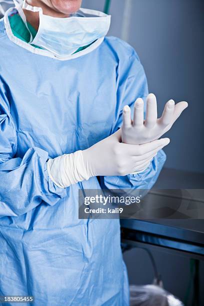 medical worker putting on latex gloves - operating gown stock pictures, royalty-free photos & images