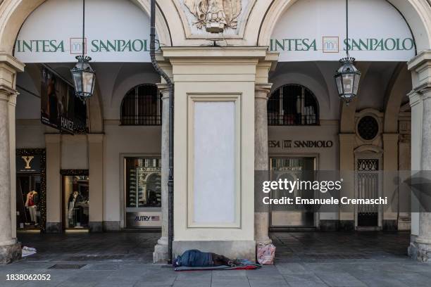 Homeless person sleeps on the ground in front of the headquarters of Intesa Sanpaolo banking group located in Piazza San Carlo, on December 07, 2023...