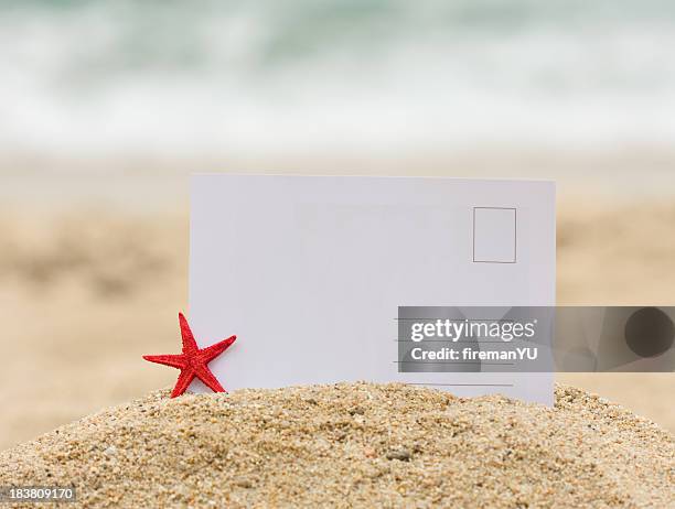 blank postcard stuck in mound of sand next to a starfish - paper product stockfoto's en -beelden