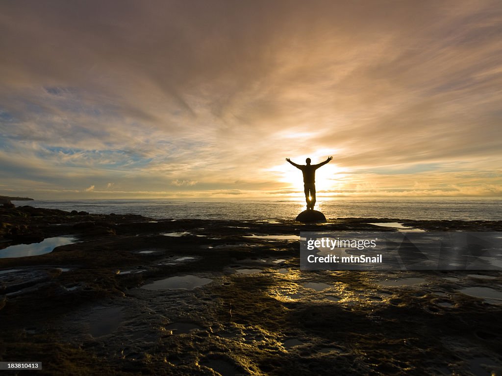 Silhouetted with arms raised on rocky beach at sunrise