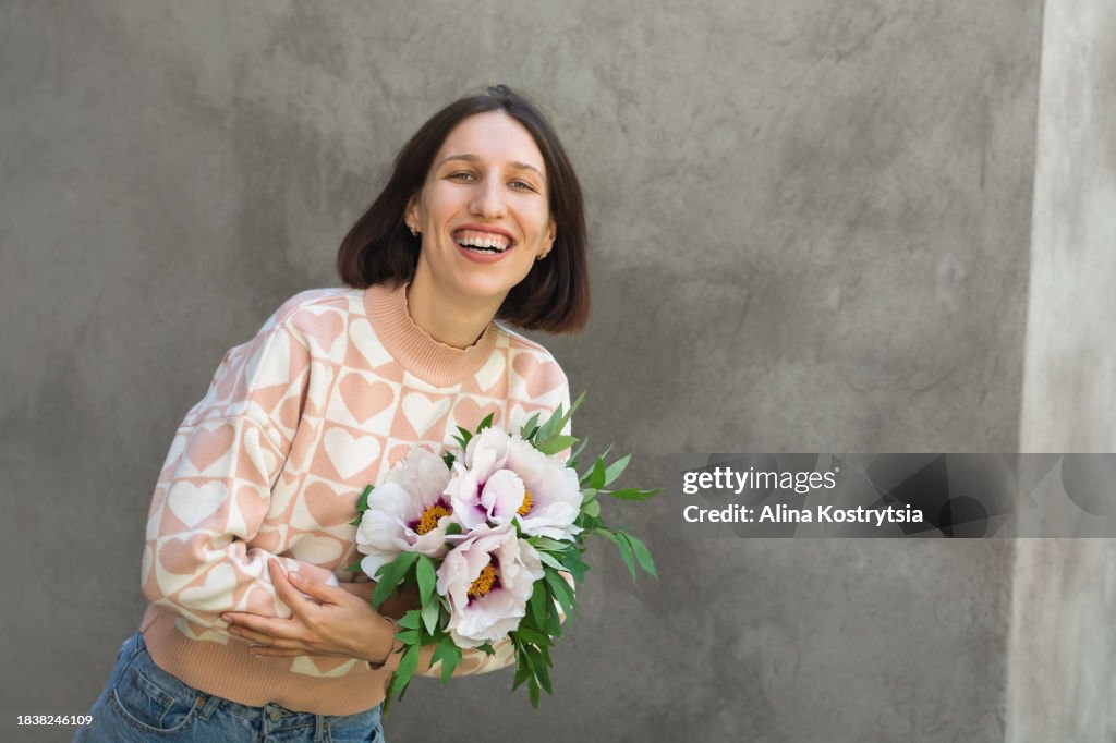 Smiling woman with bouquet of white peonies on gray background