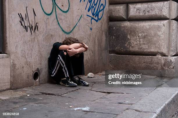 boy huddled and alone on city street - starving children 個照片及圖片檔