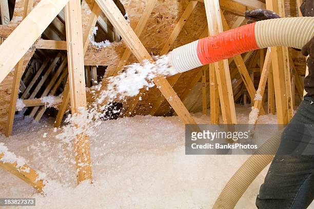 worker spraying blown fiberglass insulation between attic trusses - isolatiemateriaal stockfoto's en -beelden
