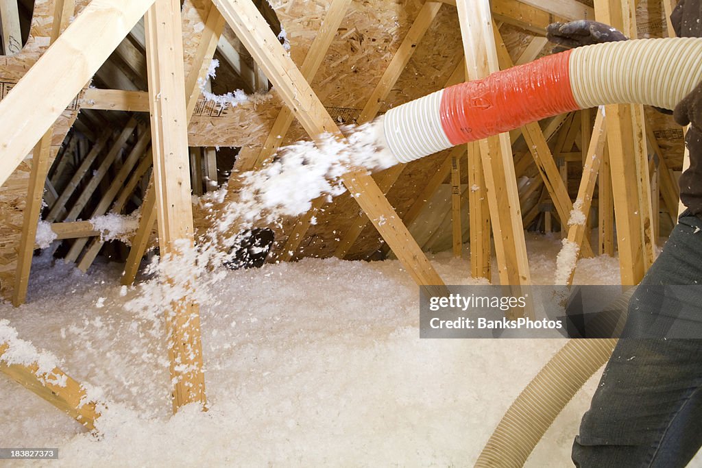 Worker Spraying Blown Fiberglass Insulation between Attic Trusses