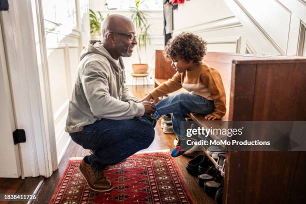 father tying toddler boy's shoes in hallway - black shoe stock pictures, royalty-free photos & images