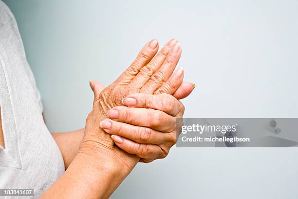 elderly woman grasping arthritic hands - rheumatism stock pictures, royalty-free photos & images