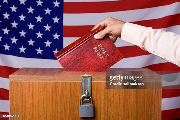 mano humana insertar biblia a urnas antes de bandera estadounidense - cristiano fotografías e imágenes de stock