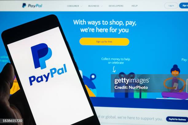 The PayPal online banking logo is being displayed on a smartphone with the PayPal web page visible in the background, in this photo illustration, in...