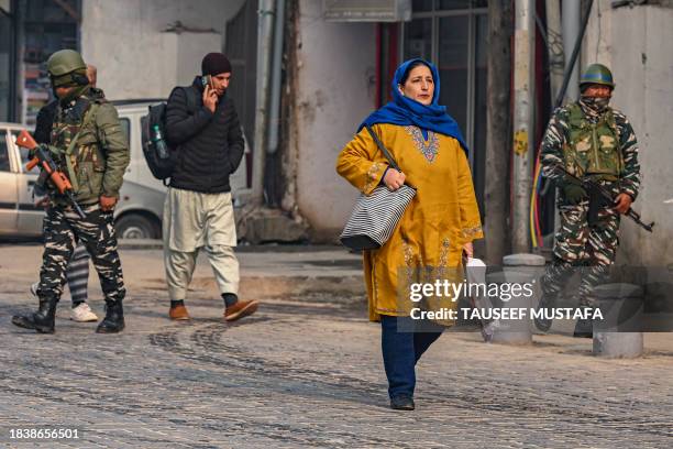 People walk along a street as Indian paramilitary personnel patrol in Srinagar on December 11 ahead of Supreme Court's verdict on Article 370....