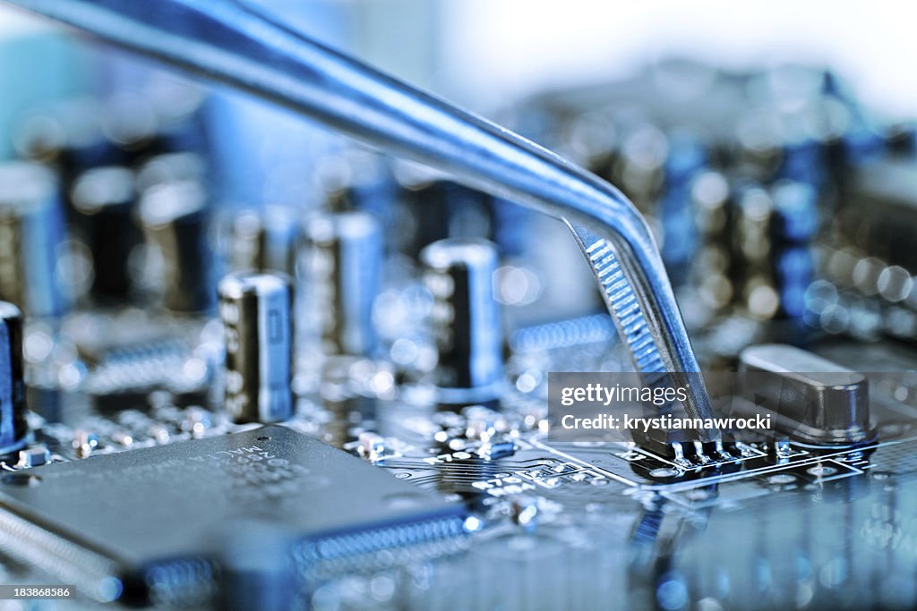 Tweezers grasping microchip on blue computer circuit board