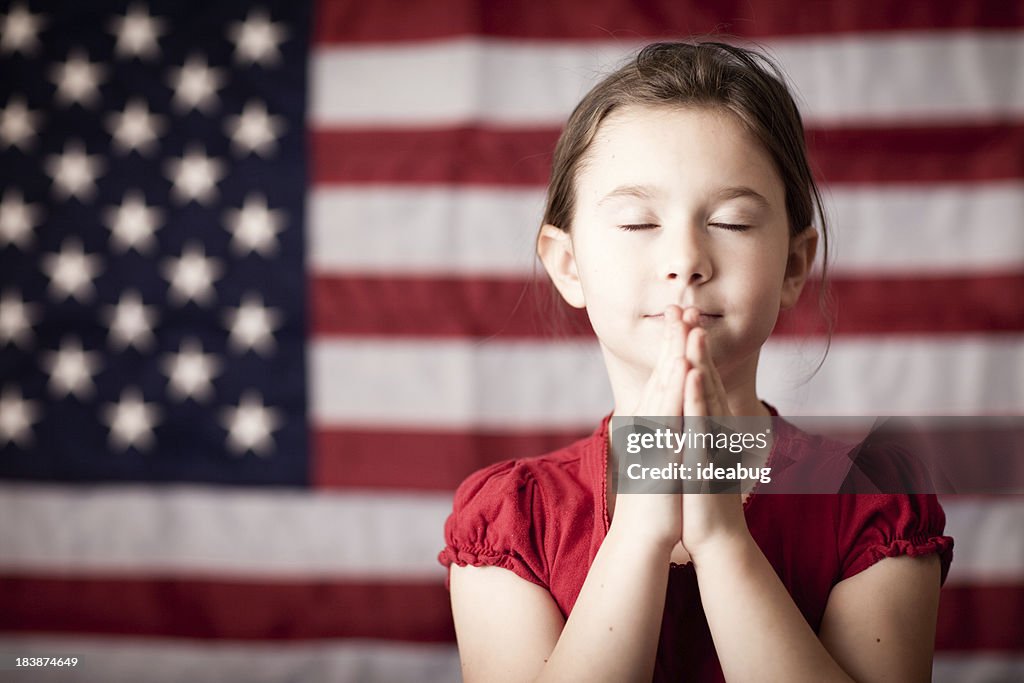 Young Girl Folding Hands and Praying by American Flag
