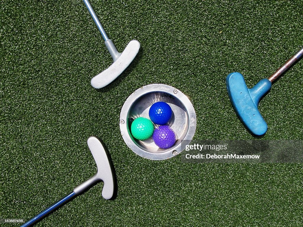 Trois coloré balles de Golf et Putting de fer entourent Astroturf trou