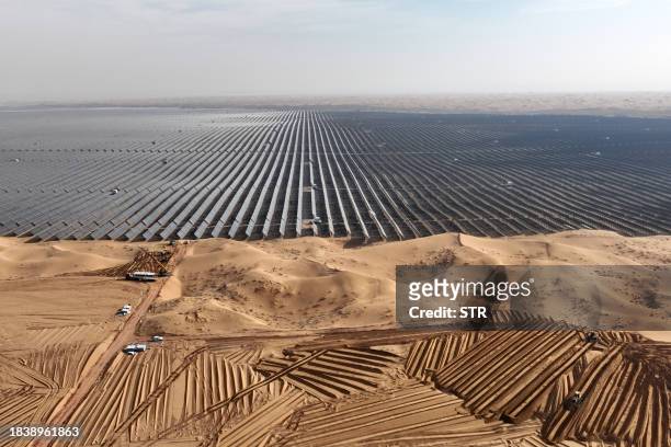 In this photo taken on December 9 vehicles prepare land for new solar panels next to a field of solar panels during construction at the Ningxia...