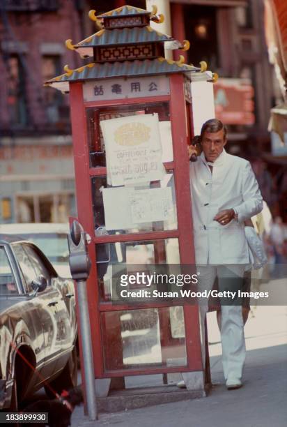 Portrait of German-born American fashion designer John Weitz dressed in one of his designs, a white suit with toggle fasterners, as he makes a call...