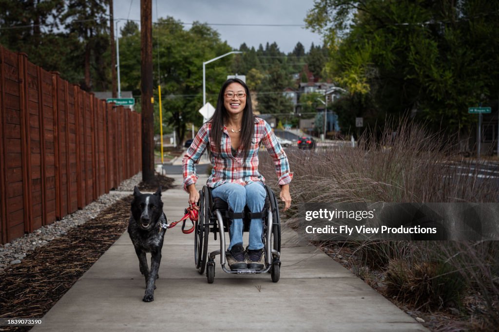 Active Asian woman using a wheelchair while taking her pet dog for a walk
