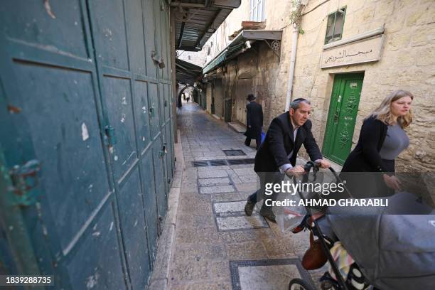 People walk past closed shops during a general strike in the Old City of Jerusalem on December 11 during a general strike in solidarity with Gaza,...