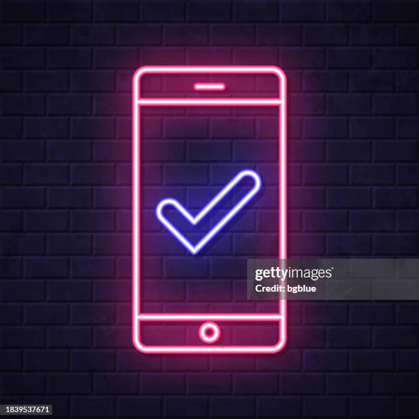 smartphone with check mark. glowing neon icon on brick wall background - looking over wall stock illustrations