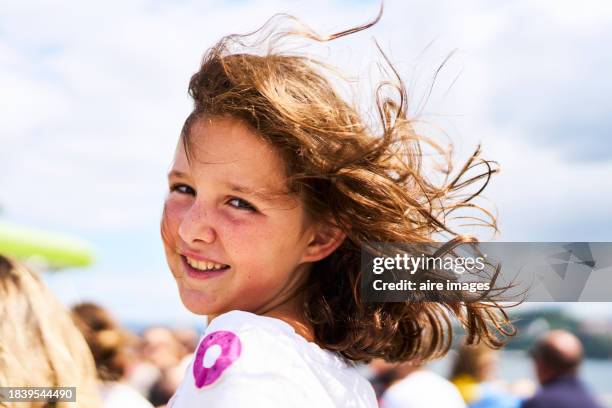 a beautiful girl smiling at the camera seen in profile her brown hair is in motion and illuminated by the sun's rays. - vigo stock pictures, royalty-free photos & images