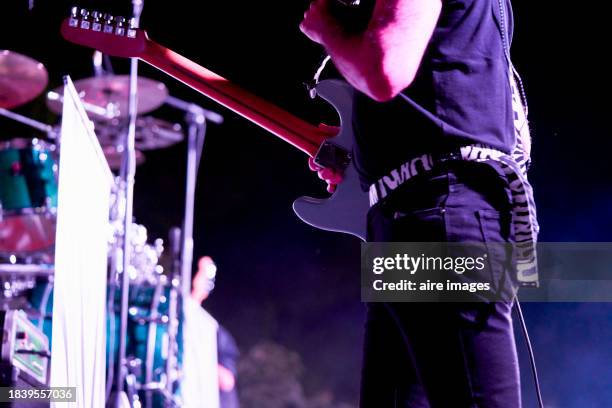 close-up of rear view of midsection of a performer standing playing his guitar in front of the blurry audience in a concert - electric guitarist stock pictures, royalty-free photos & images