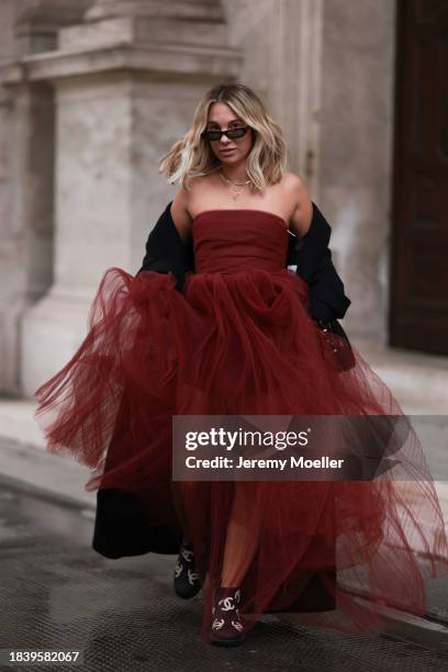 Karin Teigl seen wearing Saint Laurent brown tortoise sunglasses, H&M Studio red ruffled tulle long bandeau dress, gold necklaces, H&M black wool...