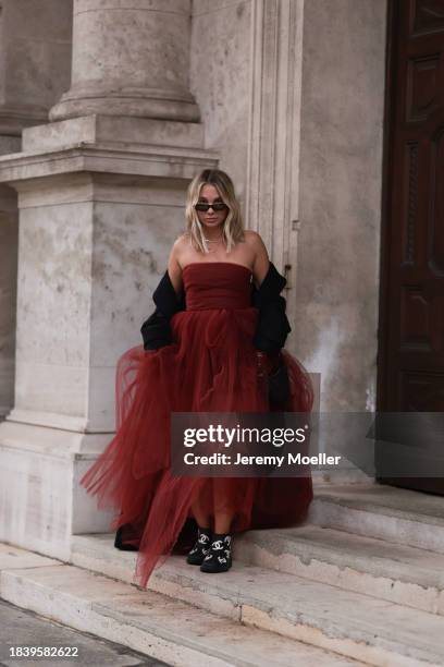 Karin Teigl seen wearing Saint Laurent brown tortoise sunglasses, H&M Studio red ruffled tulle long bandeau dress, gold necklaces, H&M black wool...