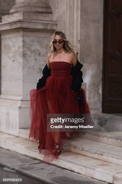 Karin Teigl seen wearing Saint Laurent brown tortoise sunglasses, H&M Studio red ruffled tulle long bandeau dress, gold necklaces, H&M black wool...