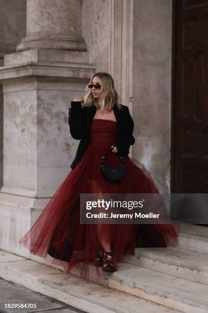 Karin Teigl seen wearing Saint Laurent brown tortoise sunglasses, H&M Studio red ruffled tulle long bandeau dress, gold necklaces, H&M black wool...