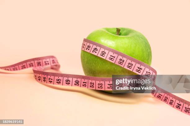 measuring tape wrapped around a green apple against  trendy beige orange pink peach color background. - centimeter stock pictures, royalty-free photos & images