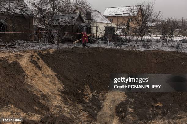 Communal worker walks next to a crater and destroyed houses following a Russian shelling in Kyiv, on December 11 amid the Russian invasion of...