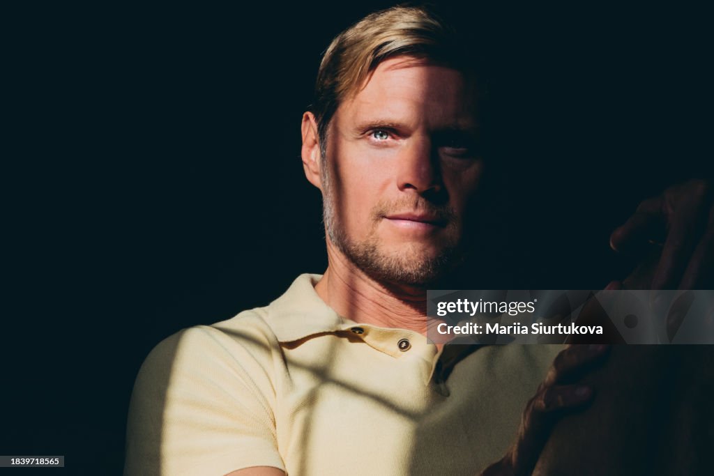 High contrast portrait of handsome bearded middle aged man with natural sun lighting on his face on dark background.