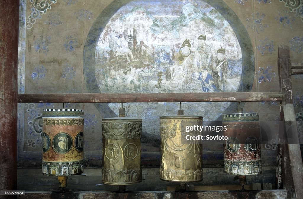 Old prayer wheels in front of a mural at Ta Er Si - Kumbum - Xining - Qinghai Province, China, Tibet